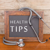 blackboard with text "Health tips" and stethoscope on wooden background
