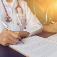 Physician doctor writing on medical health care record, patients discharge, or prescription form paperwork in hospital clinic discussing success medical healthcare, Medicine doctor's working concept