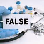 Medicine and health concept. A stethoscope and ampoules lie on a white background, the doctor holds a business card with the inscription - FALSE Medicine and health concept. A stethoscope and ampoules lie on a white background, the doctor holds a business card with the inscription - FALSE