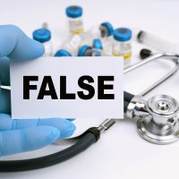 Medicine and health concept. A stethoscope and ampoules lie on a white background, the doctor holds a business card with the inscription - FALSE Medicine and health concept. A stethoscope and ampoules lie on a white background, the doctor holds a business card with the inscription - FALSE