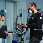 Medical doctors in sports science lab measuring performance cardiorespiratory of athlete. Team of researcher monitoring vo2 of sportsman running on cross trainer equipped with electrodes and mask