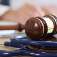 Closeup of judge gavel of stethoscope doctor in background writing notes. Concept of legal aspects of healthcare and medical insurance payments