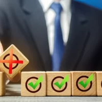 Business professional pointing to red cross block among green checkmark blocks symbolizing decision success and failure