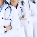 Group of modern doctors standing as a team with arms crossed in hospital office. Physicians ready to examine and help patients.